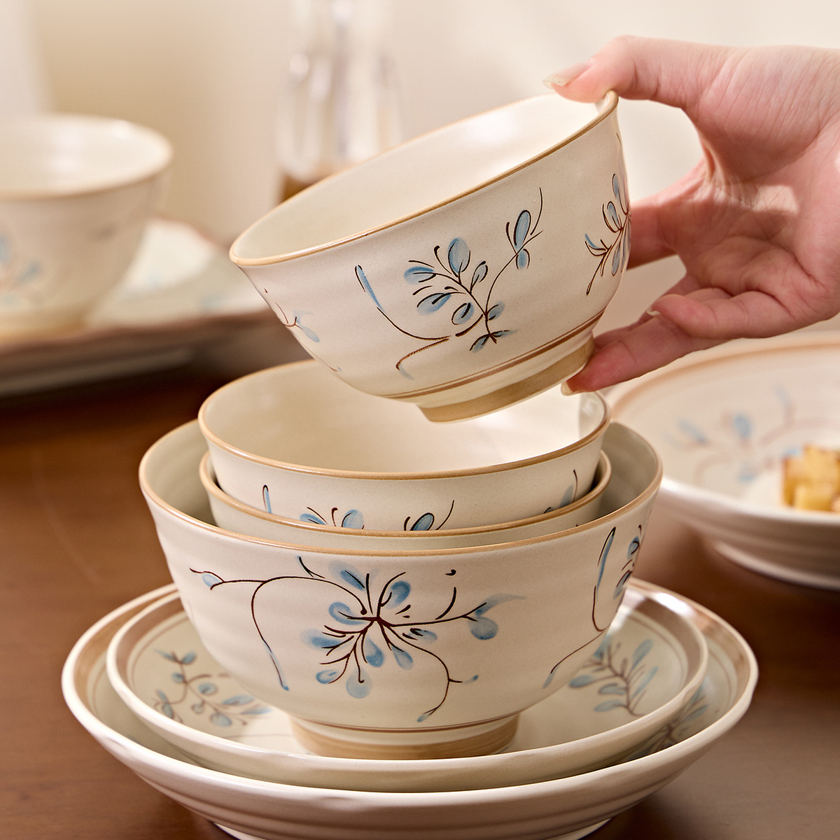 Simple Retro rice bowls and plates stacked on a wooden table, one bowl lifted by hand. Food and props not included.