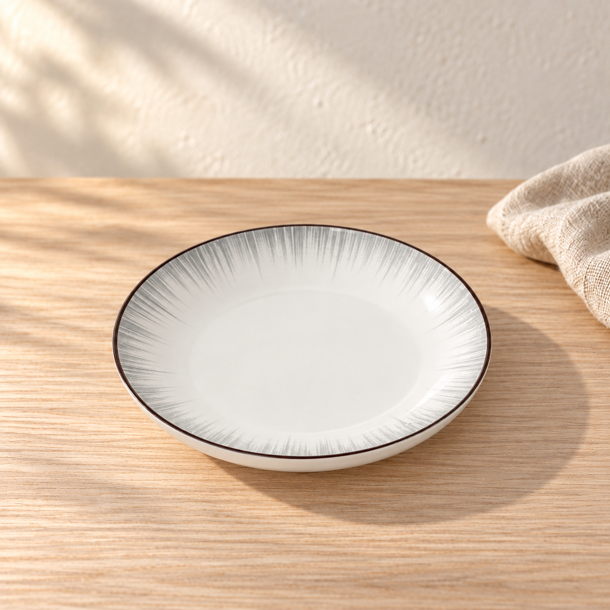 A pale celadon 7 inch plate with fine grey brush strokes radiating from the centre, on a light wood table in afternoon light.