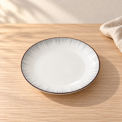 A pale celadon 8 inch plate with fine grey brush strokes radiating from the centre, on a light wood table in afternoon light.