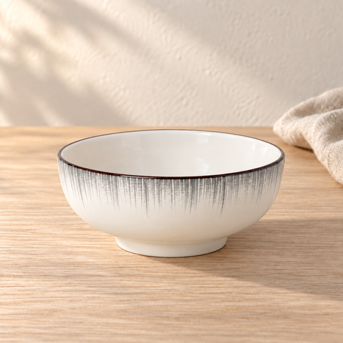 A pale celadon 8 inch soup bowl with fine grey brush strokes below the rim, on a light wood table in afternoon light.
