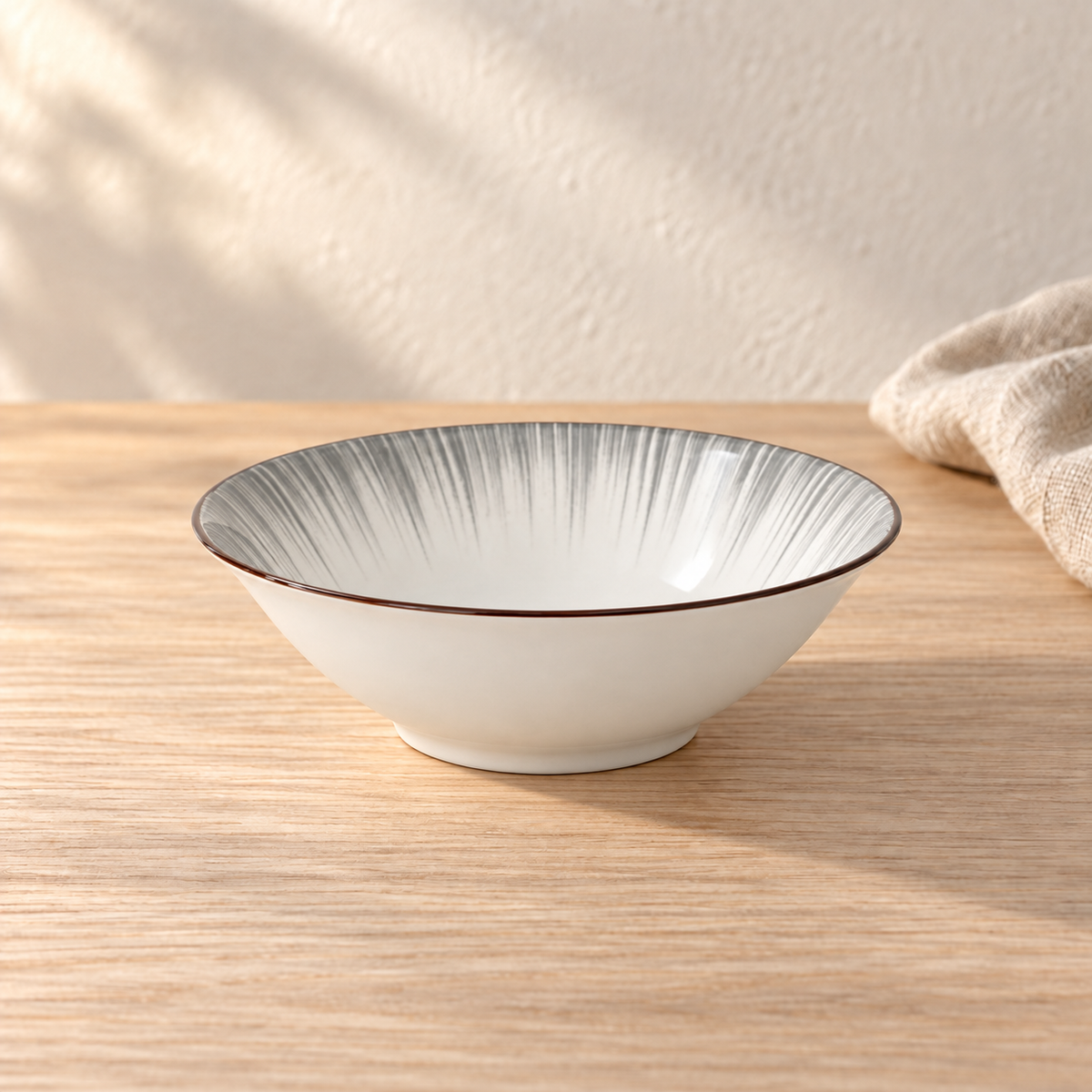 A pale celadon 8 inch flared bowl with fine grey brush strokes, on a light wood table in afternoon light.