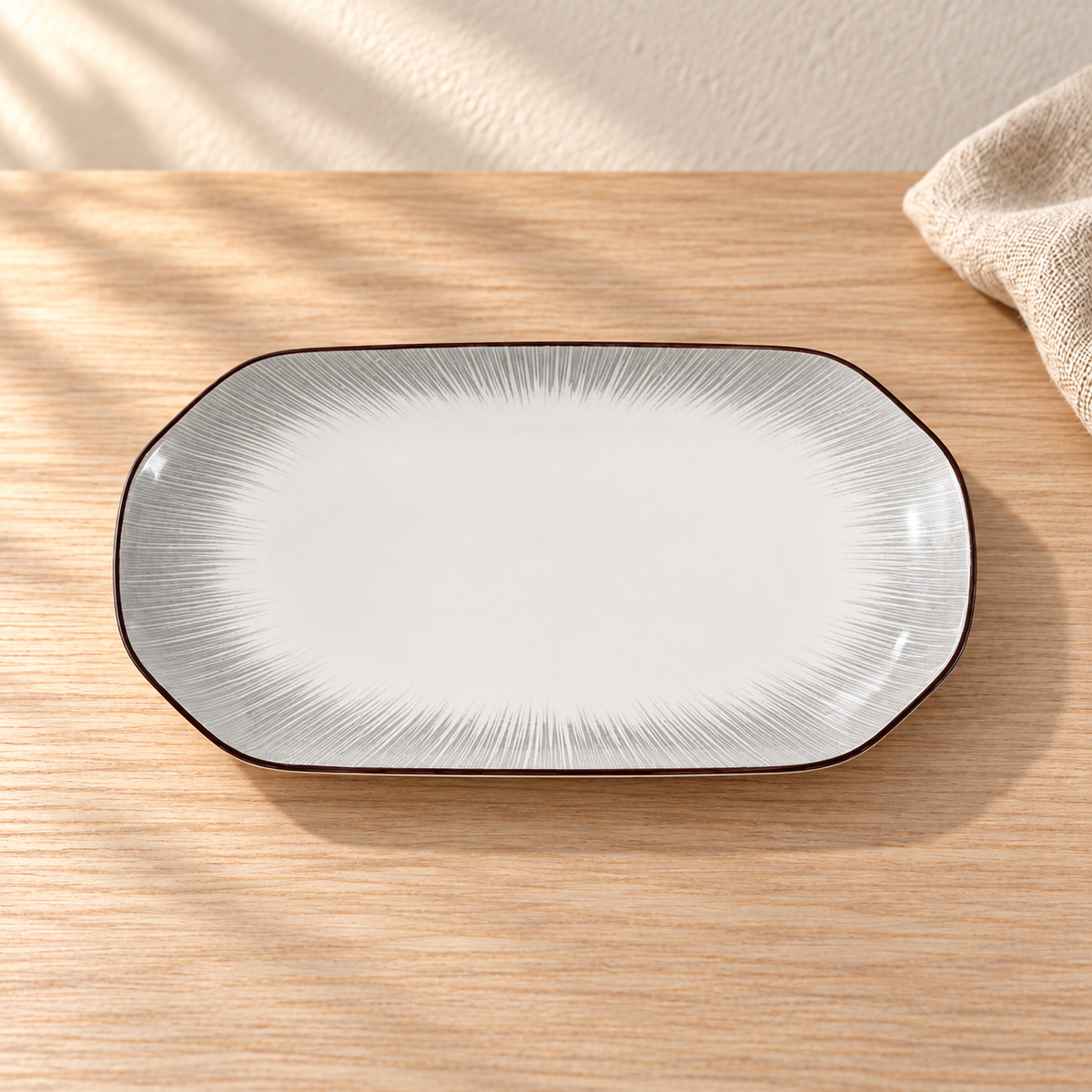A pale celadon 12 inch oval fish platter with fine grey brush strokes, on a light wood table in afternoon light.