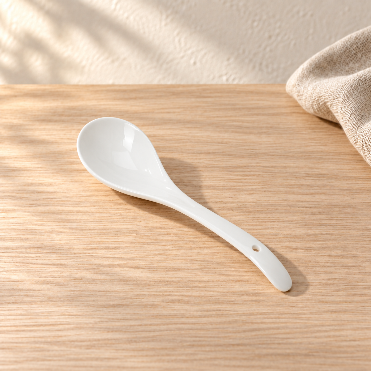 A pale celadon serving spoon, on a light wood table in afternoon light.