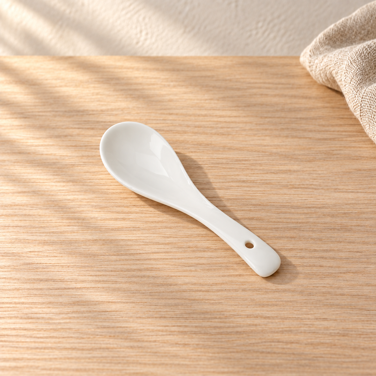 A small pale celadon spoon, on a light wood table in afternoon light.