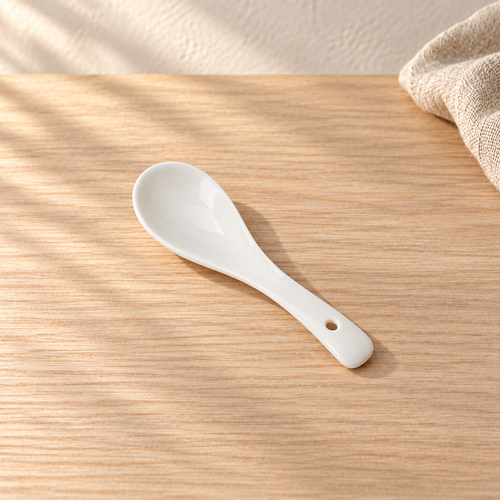A small pale celadon spoon, on a light wood table in afternoon light.