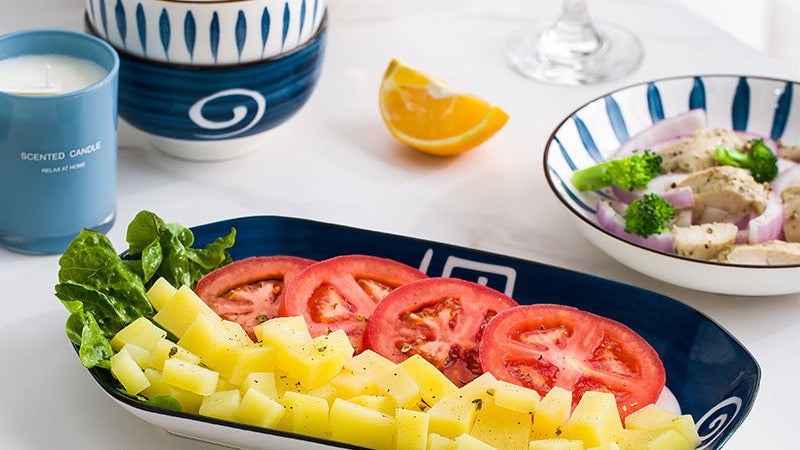 Oval navy platter with tomato, potato, and greens on a marble table.