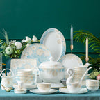 The set arranged on a dark green table with candles and flowers, showing the plates, bowls, teapot and cups together