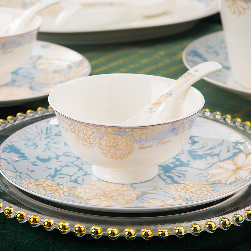 A footed rice bowl and spoon resting on a dinner plate, showing the blue and gold floral rim pattern
