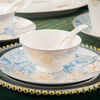 A footed rice bowl and spoon resting on a dinner plate, showing the blue and gold floral rim pattern
