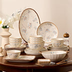 The full set displayed on a round wooden table, an oval platter and a dinner plate standing upright behind stacked bowls, small dishes, a rectangular tray and a chopstick rest.