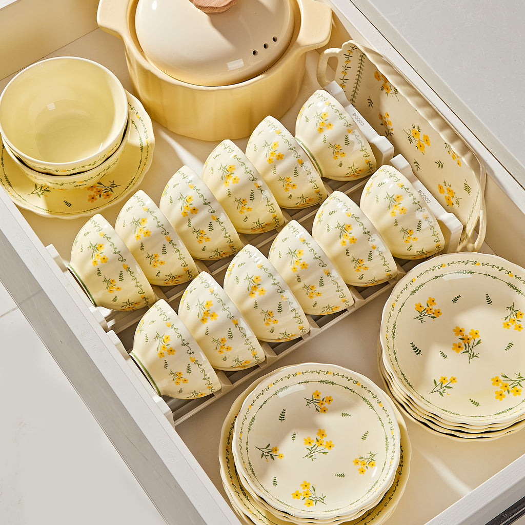 The cream set with small yellow flowers laid out in an open kitchen drawer: rows of rice bowls in a rack, stacked plates, a lidded casserole and a handled serving tray.
