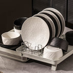 White and black plates and bowls from the range standing in a dish rack on a kitchen counter.
