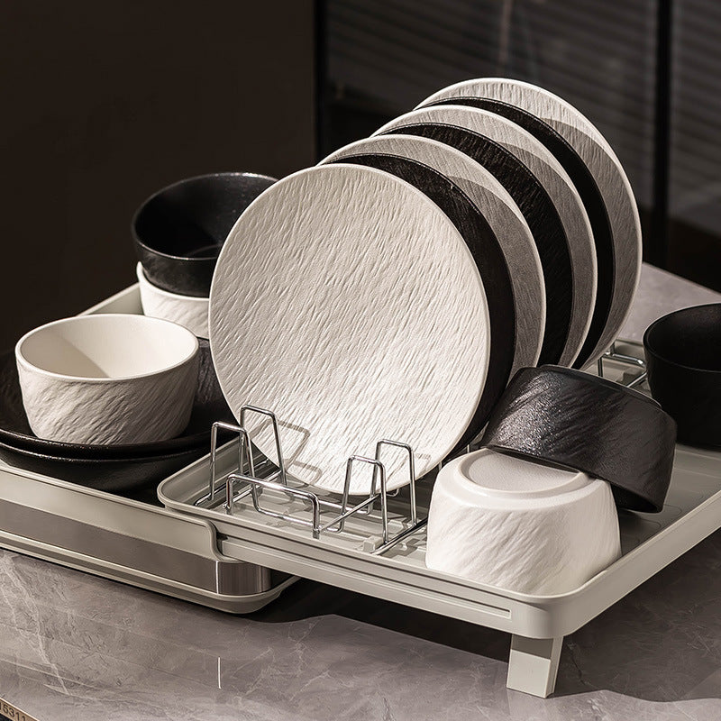 White and black plates and bowls from the range standing in a dish rack on a kitchen counter.