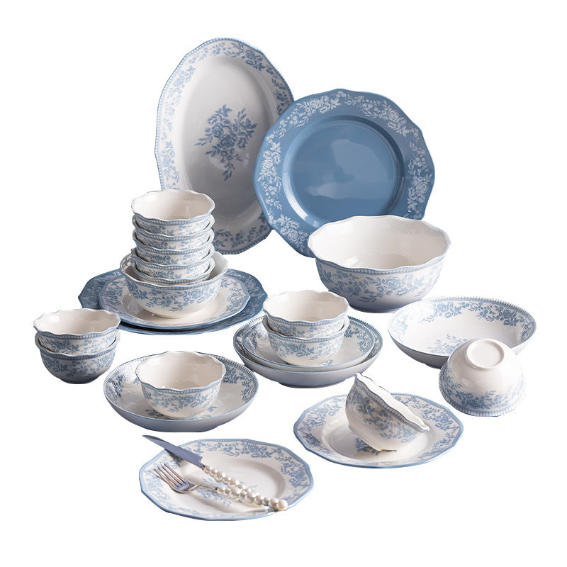 The blue and white set arranged on a white background: scallop-edged plates with a floral border, stacked bowls, an oval platter, a solid blue plate, a gravy boat and small dishes.