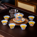 The tea set on a dark wood table: the lidded tea bowl on its saucer standing on a scalloped tray, six matching cups filled with tea and a clear glass pitcher.