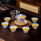 The tea set on a dark wood table: the lidded tea bowl on its saucer standing on a scalloped tray, six matching cups filled with tea and a clear glass pitcher.