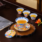 A filled cup on its matching saucer standing on a woven tray, the lid resting beside it and three more filled cups behind.