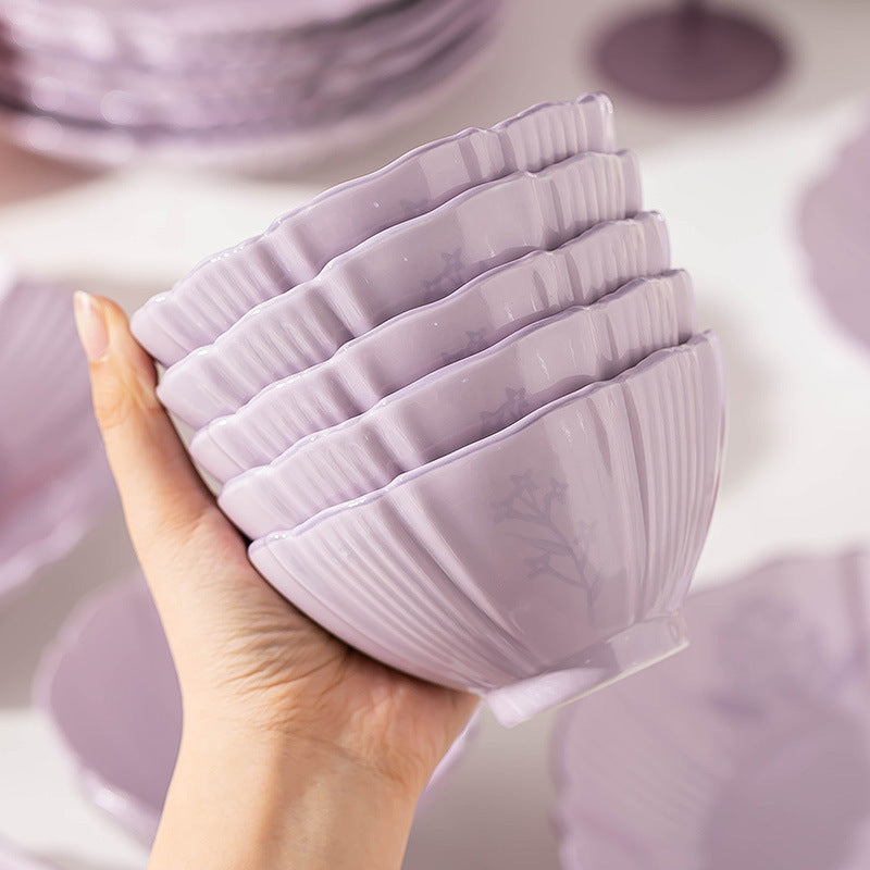 A hand holds a stack of five lilac fluted bowls, showing the ribbed sides and the faint floral relief.