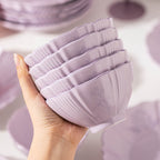 A hand holds a stack of five lilac fluted bowls, showing the ribbed sides and the faint floral relief.