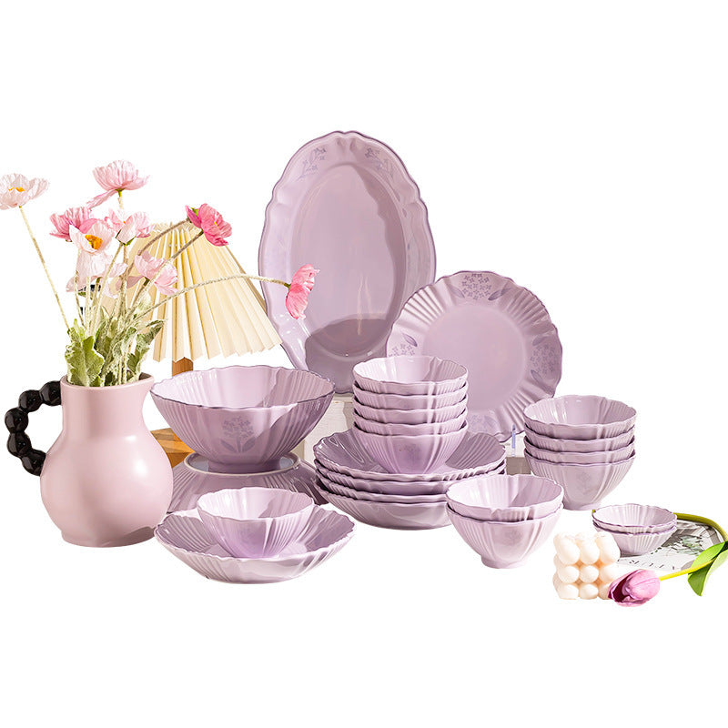 The lilac set arranged on a white background: a scallop-edged oval platter, a dinner plate, fluted bowls in several sizes and small dishes, all with a faint floral relief.