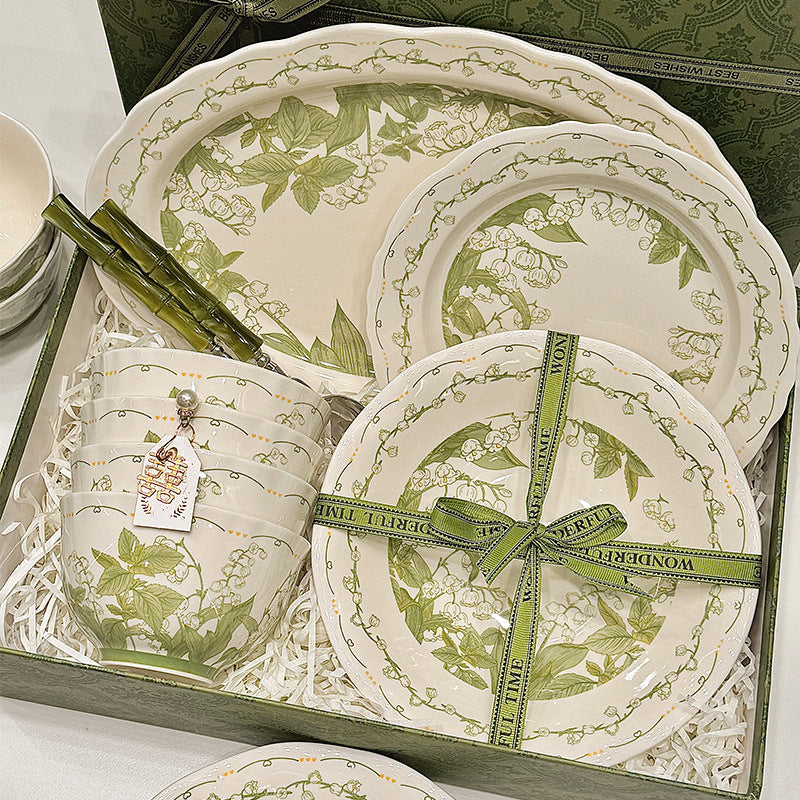 The set packed in a green gift box with paper shred and printed ribbon, plates on top and stacked bowls beside them.