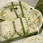 Bowls and plates tied with printed ribbon inside an open gift box, seen from above.