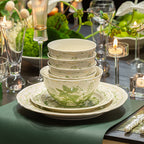 Stacked bowls on layered plates on a dark table set with candles and glassware, a green runner underneath.