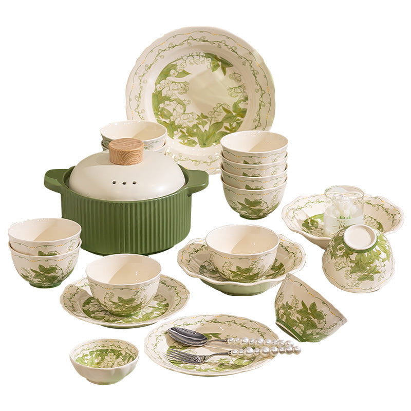 The green and cream set arranged on a white background: plates and bowls printed with lily of the valley, a lidded casserole with a wooden knob, small dishes and a lidded soup bowl.