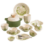The green and cream set arranged on a white background: plates and bowls printed with lily of the valley, a lidded casserole with a wooden knob, small dishes and a lidded soup bowl.