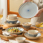 A person holds up a plate painted with radiating blue stripes above a wooden table set with matching bowls and a salad bowl.