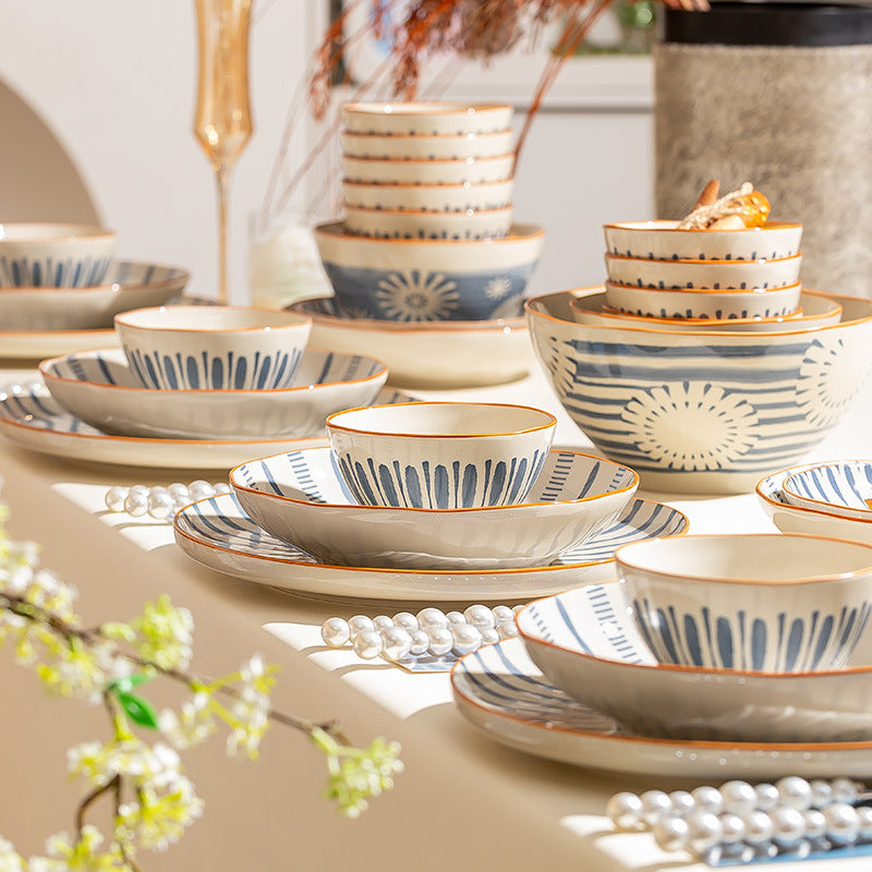 The set laid out along a cream table in soft light: stacked rice bowls, plates, a large flower-patterned bowl and shallow dishes.