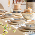 The set laid out along a cream table in soft light: stacked rice bowls, plates, a large flower-patterned bowl and shallow dishes.