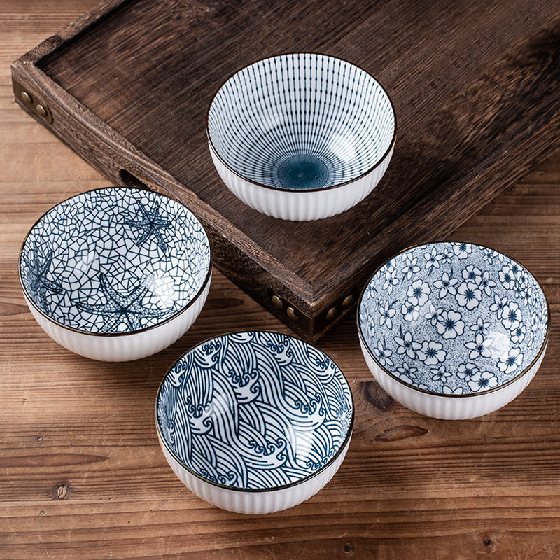 Four rice bowls in different blue and white patterns, fine stripes, crackle, small flowers and a wave scroll, on a wooden table beside a dark wooden tray.