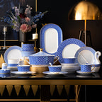 The full set displayed on a dark sideboard with a gold lamp and a flower arrangement: tureen, teapot, cups and saucers, stacked plates and an oval platter.
