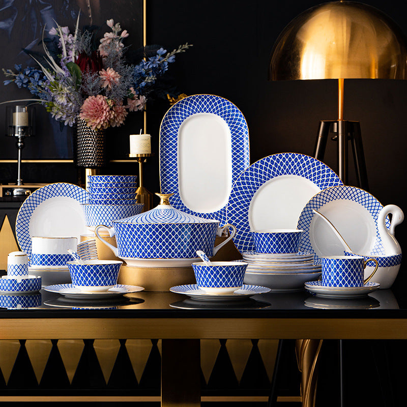 The full set displayed on a dark sideboard with a gold lamp and a flower arrangement: tureen, teapot, cups and saucers, stacked plates and an oval platter.