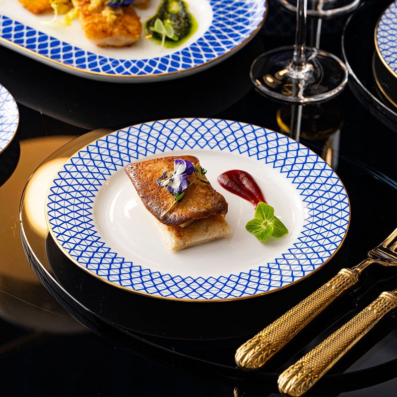 A dinner plate holding a seared fillet with garnish on a black table, gold cutlery beside it.