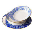 A soup plate and a dinner plate on a white background, white centres with a dense blue lattice border and a gold rim.