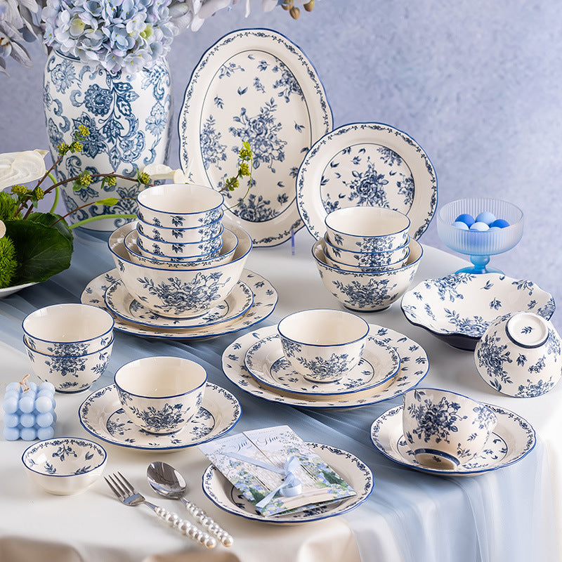 The set laid out on a white cloth beside a tall blue and white vase: stacked bowls, plates, a lidded bowl and small dishes with pearl-handled cutlery.