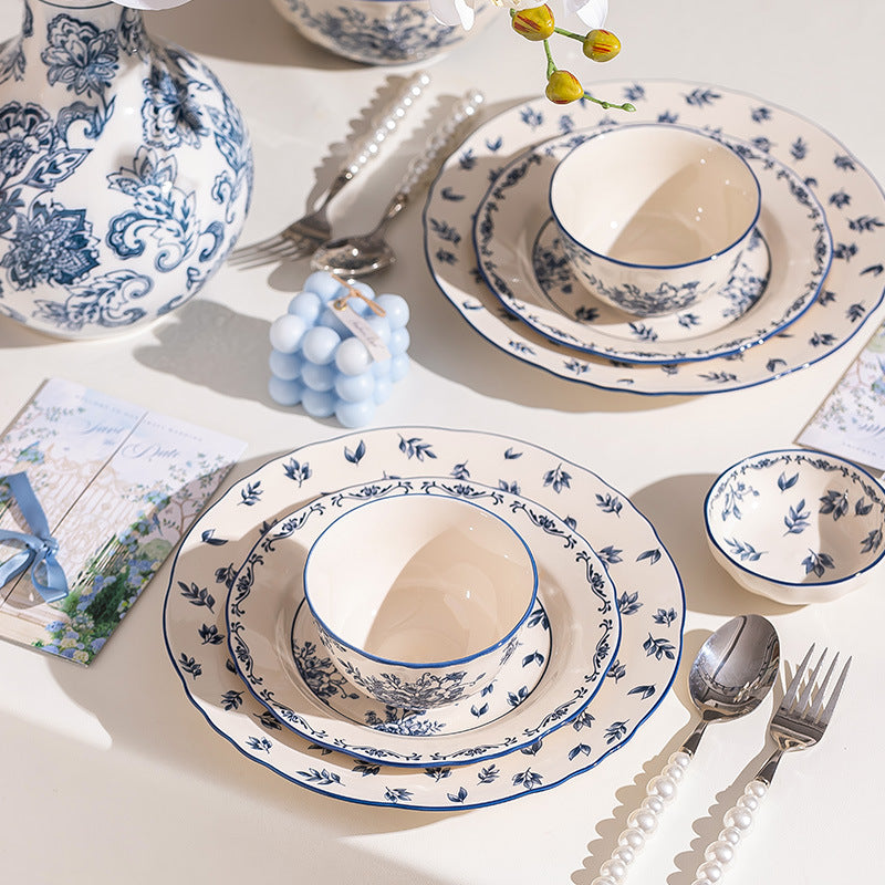 A close place setting, a bowl on layered floral plates with a small dish beside it, pearl-handled cutlery and a printed card.