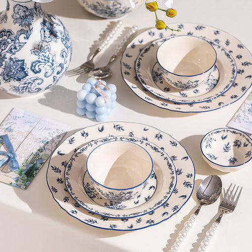 A close place setting, a bowl on layered floral plates with a small dish beside it, pearl-handled cutlery and a printed card.