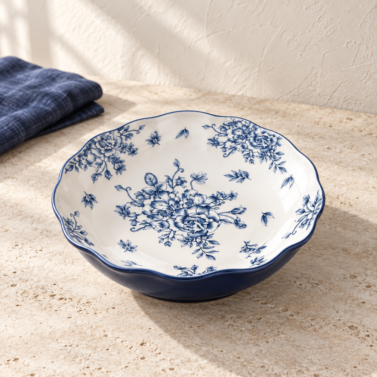 A blue and white 8 inch deep plate with a dense peony print and a deep indigo rim, on a pale limestone table in morning light.