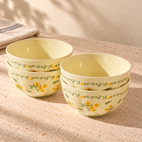Four cream 6 inch noodle bowls with a yellow flower and green vine border, stacked in two pairs on a pale stone table in morning light.