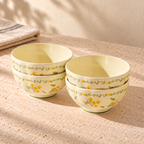 Four cream 4.5 inch rice bowls with a yellow flower and green vine border, stacked in two pairs on a pale stone table in morning light.
