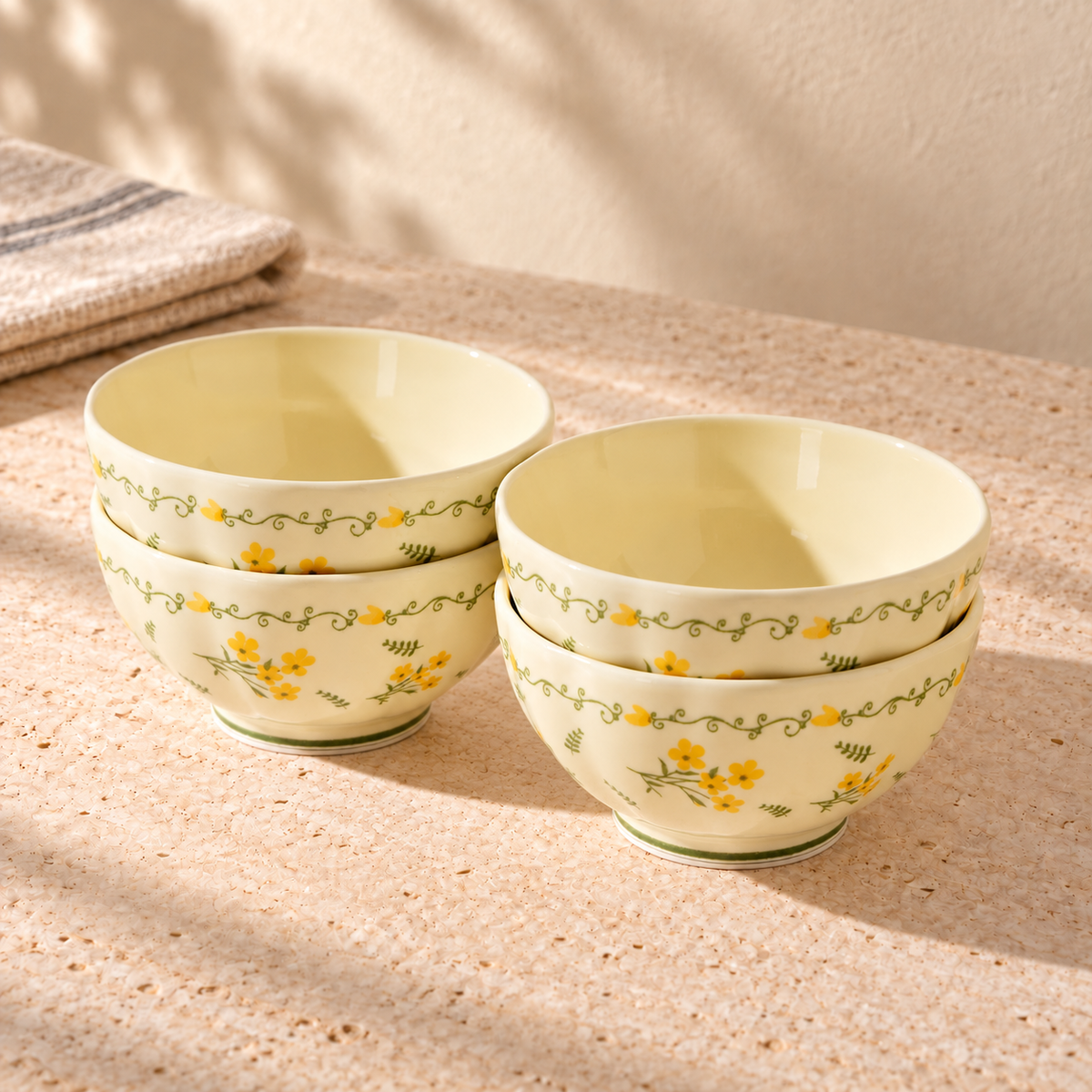 Four cream 4.5 inch rice bowls with a yellow flower and green vine border, stacked in two pairs on a pale stone table in morning light.