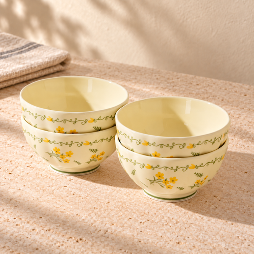 Four cream 4.5 inch rice bowls with a yellow flower and green vine border, stacked in two pairs on a pale stone table in morning light.