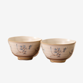 Two cream rice bowls with a small blue and brown sprig motif, shown together against a plain light background.
