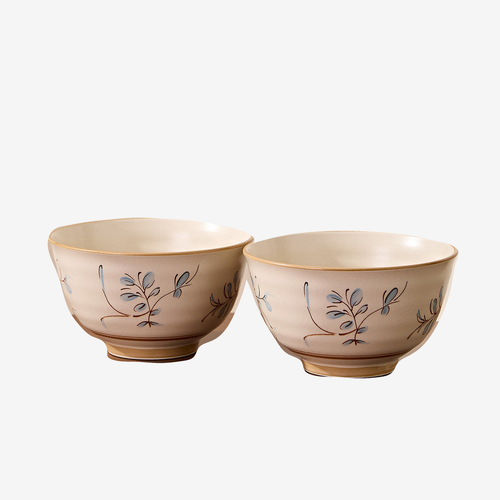 Two cream rice bowls with a small blue and brown sprig motif, shown together against a plain light background.