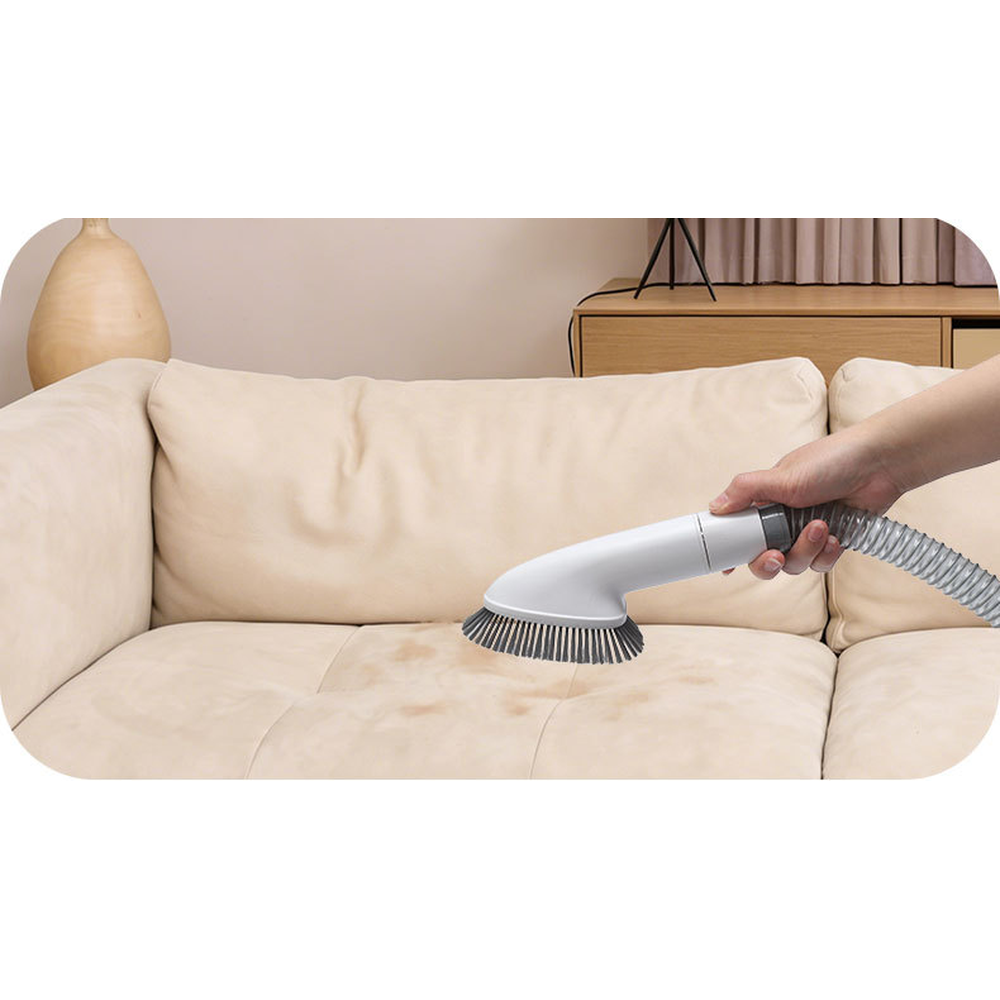 Hand using the brush nozzle of the dog grooming vacuum to pick up hair from a sofa