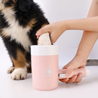 Dog's paw being dipped into the pink paw washer cup while a Bernese mountain dog puppy sits beside it