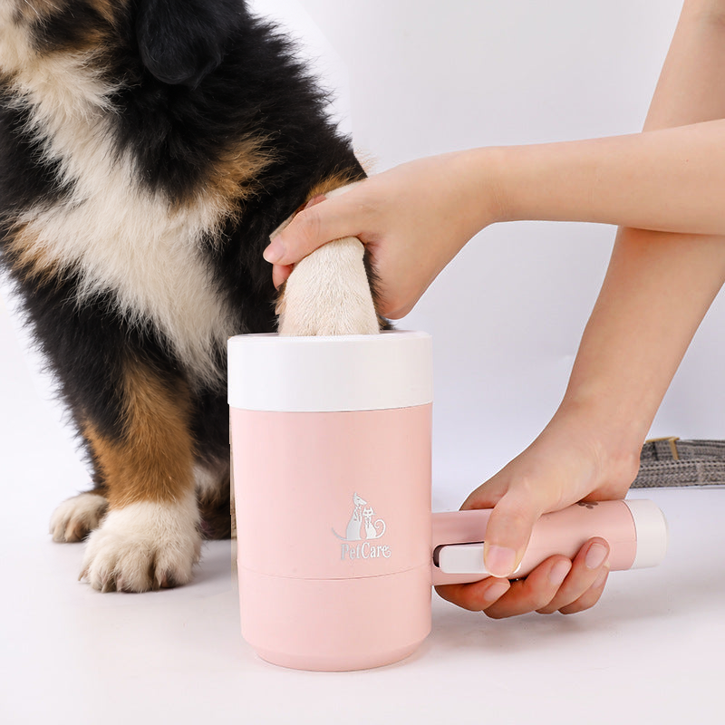 Dog's paw being dipped into the pink paw washer cup while a Bernese mountain dog puppy sits beside it